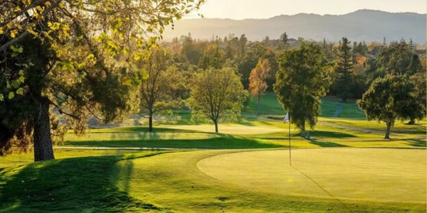 Late-afternoon fall light across a green and fairway on a Silverado golf course, with oaks and hills behind